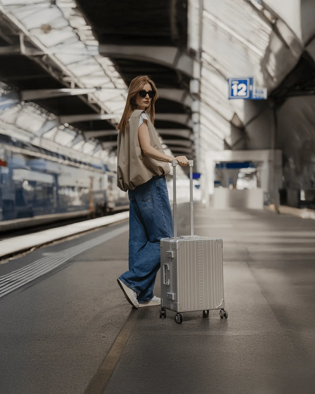 Traveler with silver Aleon aluminum carry-on luggage on a train platform.