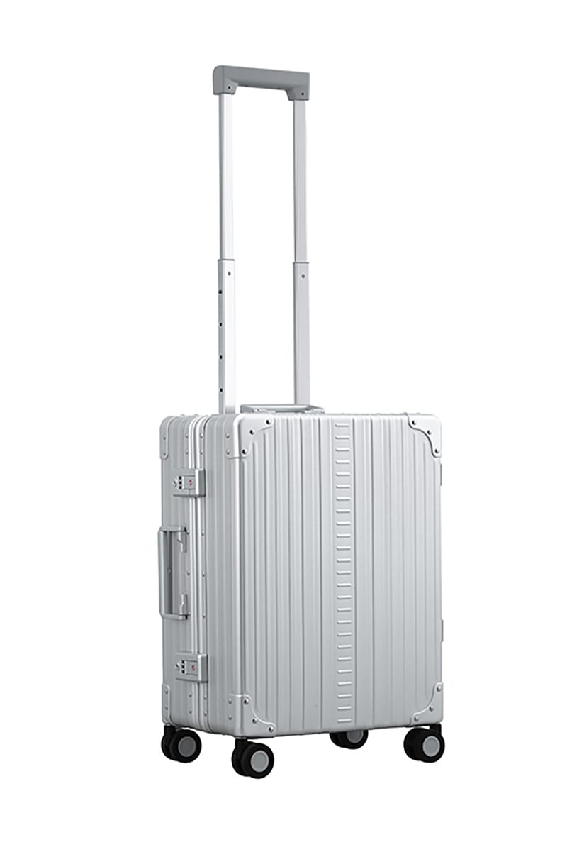 Platinum Silver Aleon aluminum luggage angled side profile showcasing full case design|The ALEON 21" Carry-On rests beside a plush airport lounge chair, its refined metallic finish complementing the sophisticated travel setting. Designed for durability and elegance, it exudes premium craftsmanship and functionality.|An open platinum ALEON 21" Carry-On reveals a neatly arranged interior with compre