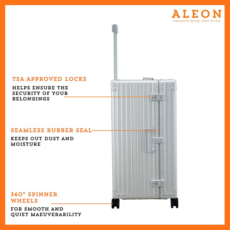 A sleek, platinum-colored aluminum trunk-style suitcase with reinforced corners and a sturdy telescoping handle. The case stands upright, showcasing its durable construction and TSA-approved combination locks.