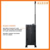 A polished onyx aluminum ALEON 21" Carry-On stands upright on a glossy airport floor, reflecting ambient lighting. Its durable, hard-shell construction and smooth wheels embody modern travel efficiency.