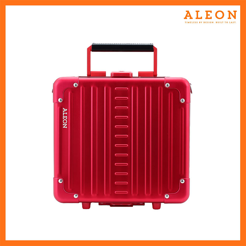 The image features a red ruby ALEON Messenger Case with a sleek, modern design. Vertical ridges run across the aluminum exterior, reinforced with metal rivets at the corners for durability. A black handle sits at the top, complementing the case’s bold aesthetic. The ALEON logo is printed in white on the left side, reinforcing brand identity. The case is set against a white background with an orange border, and the top right corner displays the ALEON logo alongside the tagline, "Timeless by design. Built to last."